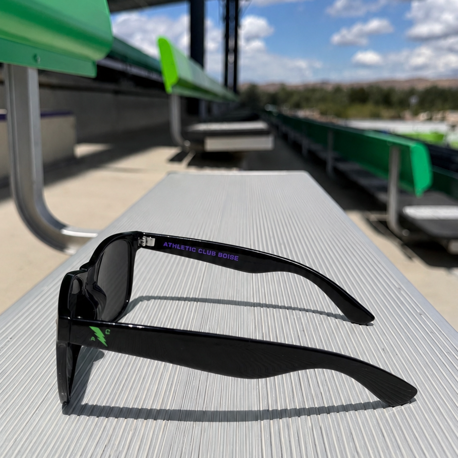 Black sunglasses on a gray surface with green seats and a cloudy sky in the background