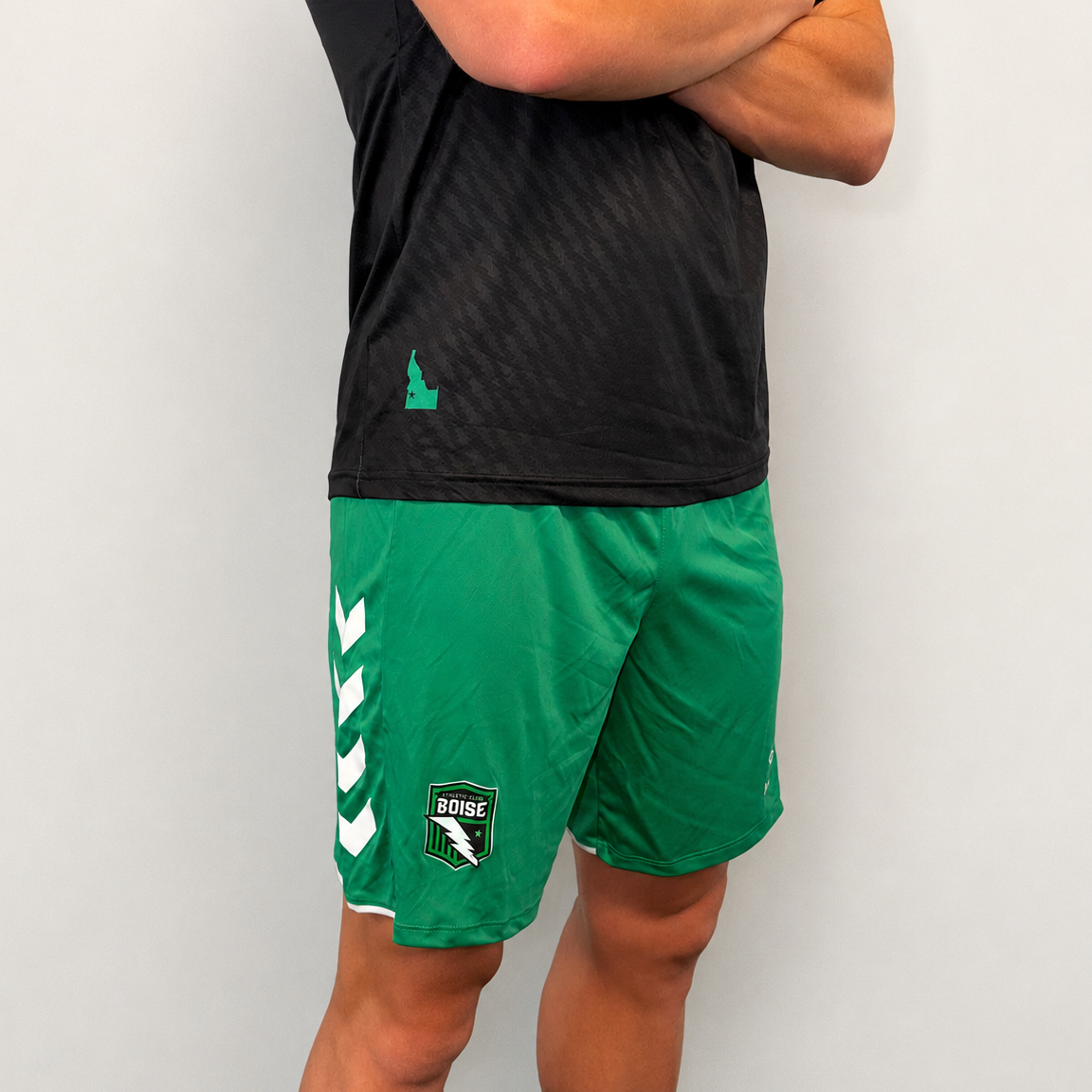 Person wearing black athletic shirt and green shorts with logos on a plain background