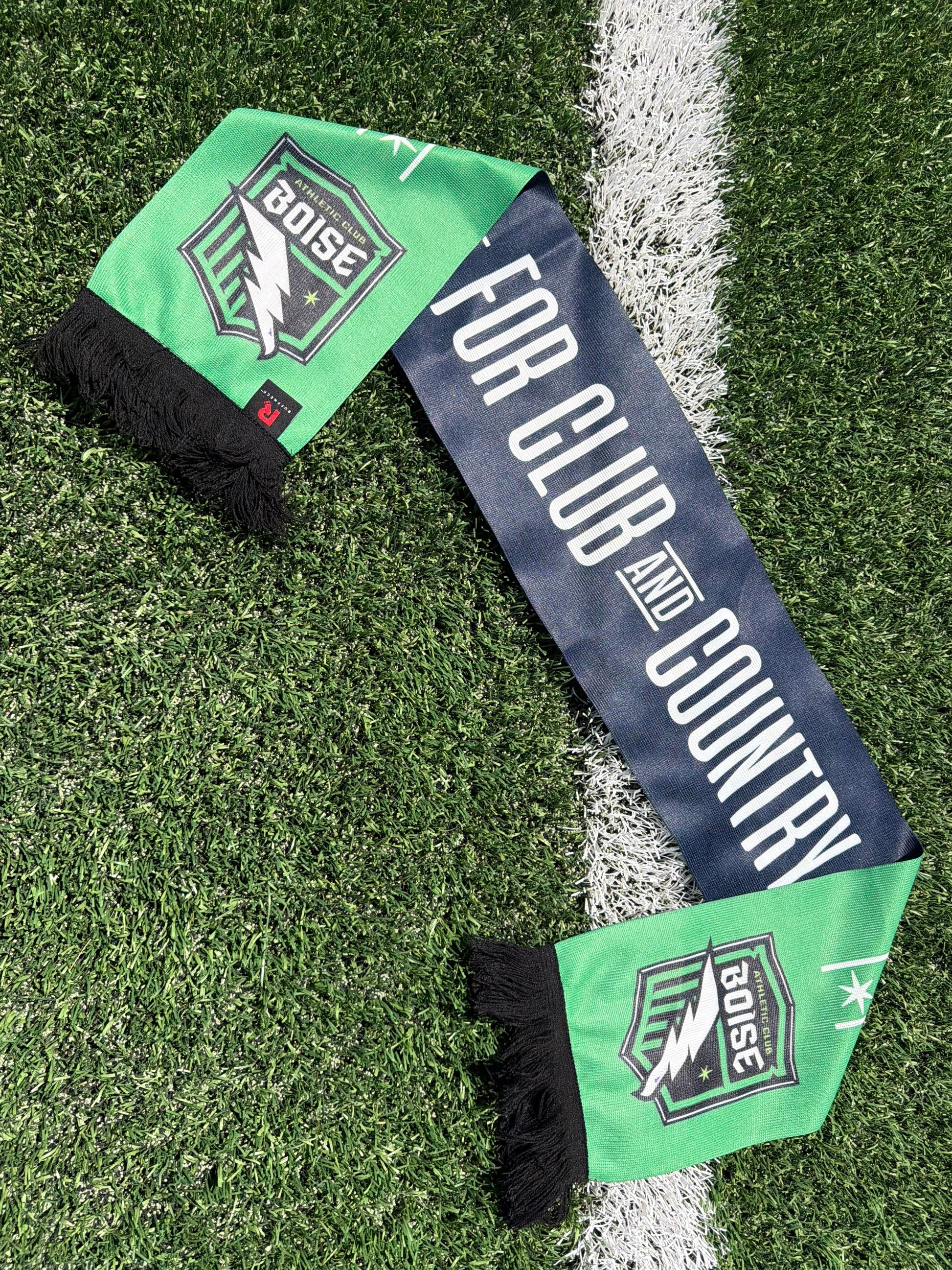 Green and blue scarf with branding on a grass field