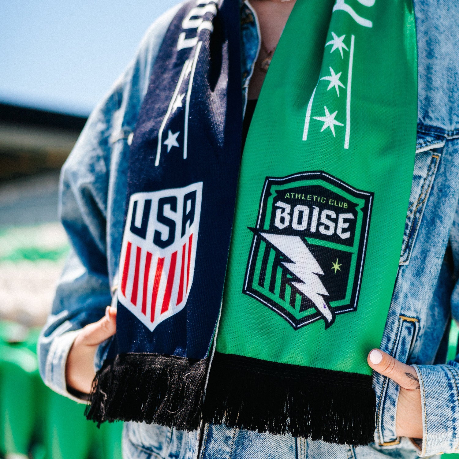 Person wearing a denim jacket with USA and Boise athletic club logos, holding a green scarf.
