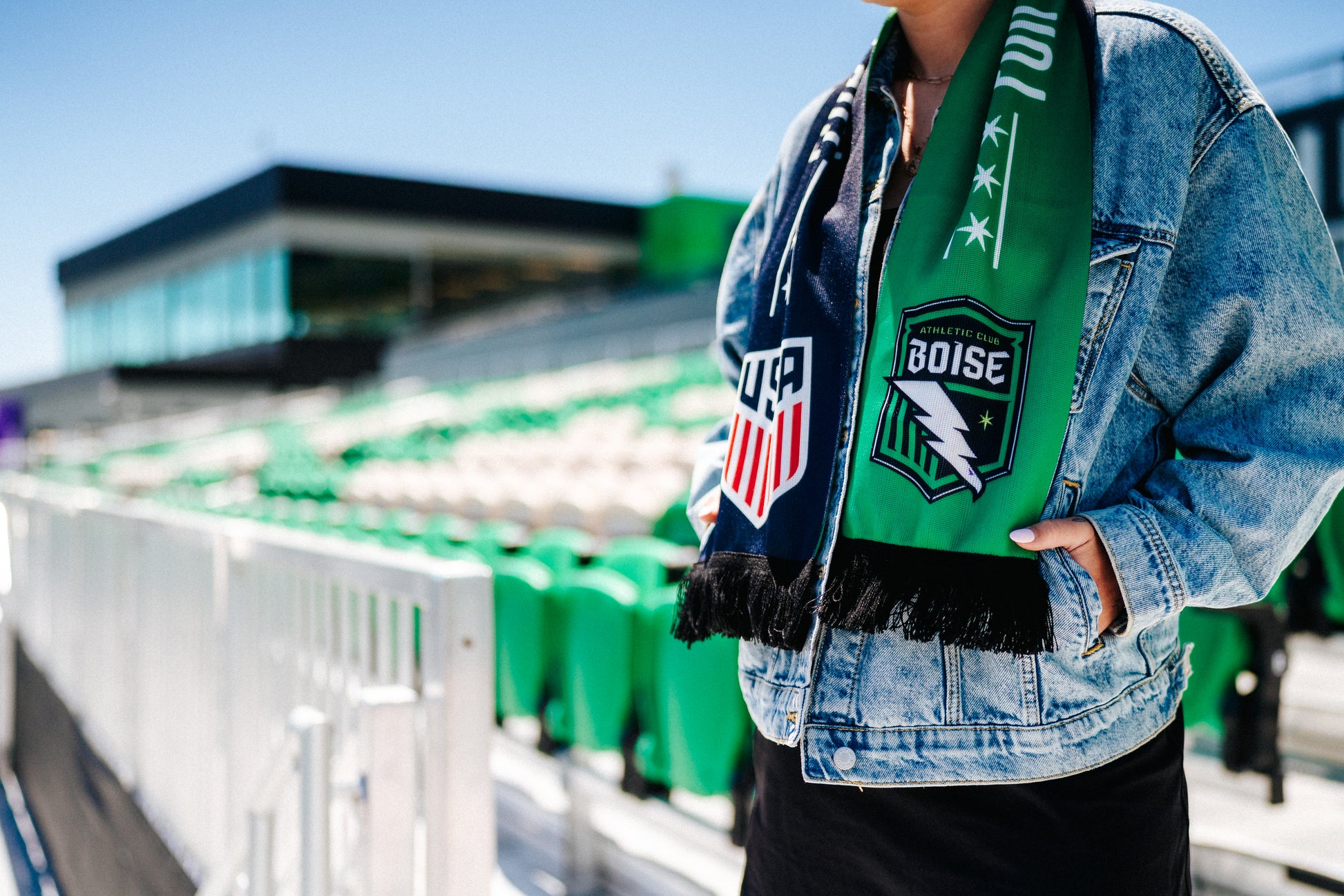 Person wearing a green scarf with a logo and text, standing in a stadium.