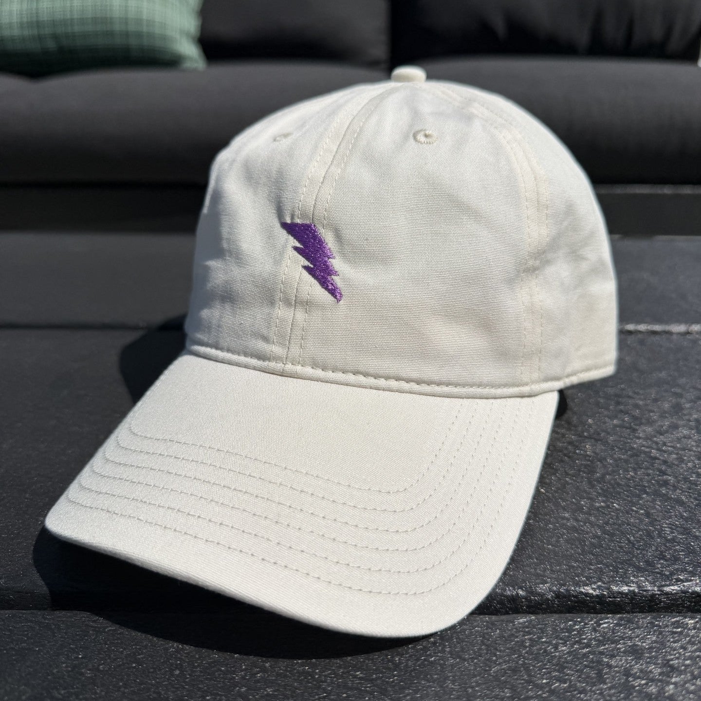 Beige cap with a purple logo on a black surface