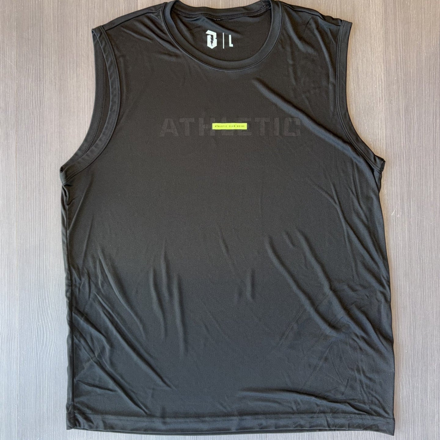 A black sleeveless athletic tank top with a small neon green vertical stripe and 'ATHLETIC' text on the chest, laid flat on a light wood floor.
